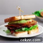 An avocado BLT on a toasted white bread on top of a white plate.