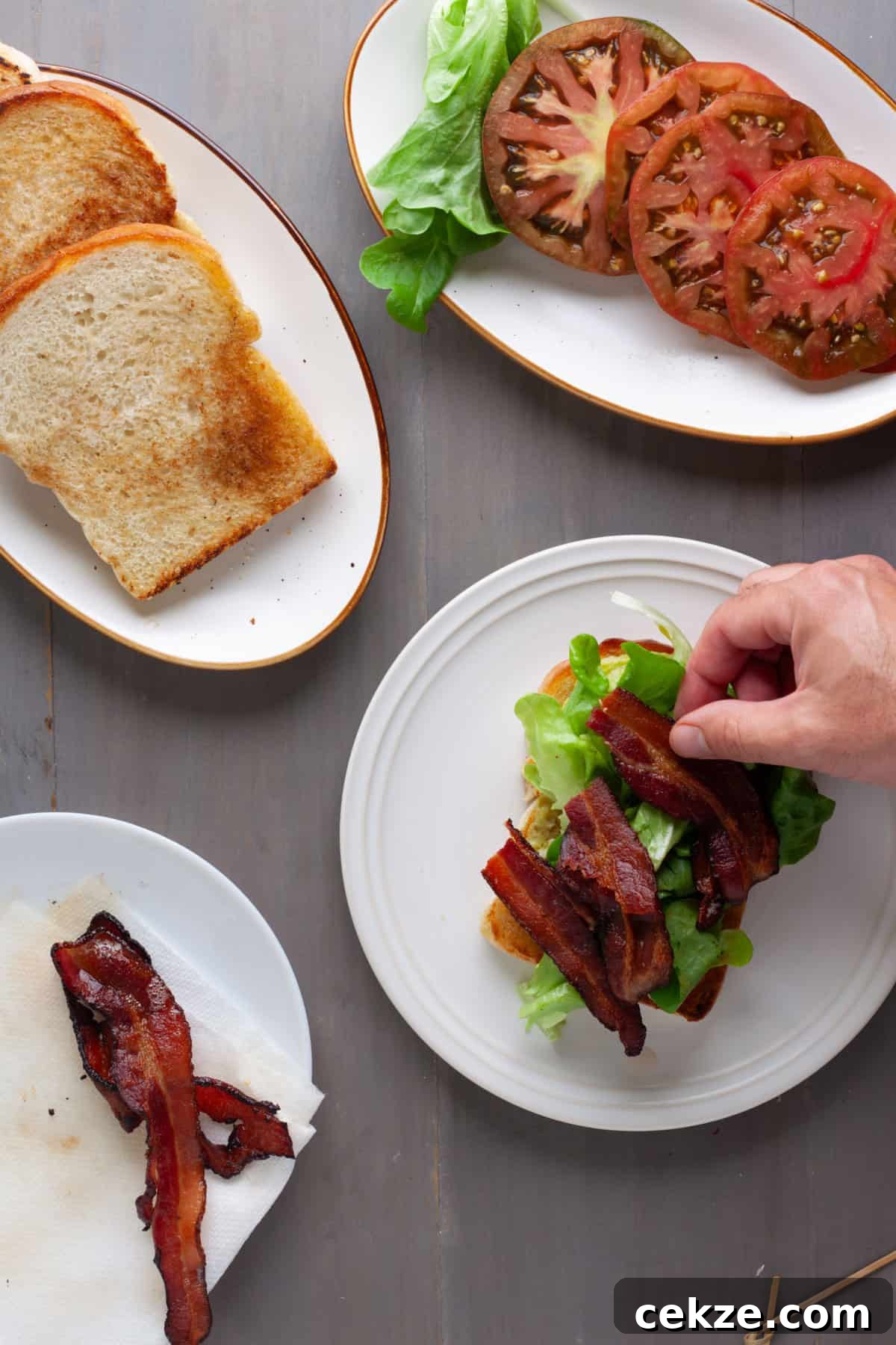 An avocado BLT getting assembled on a gray table.