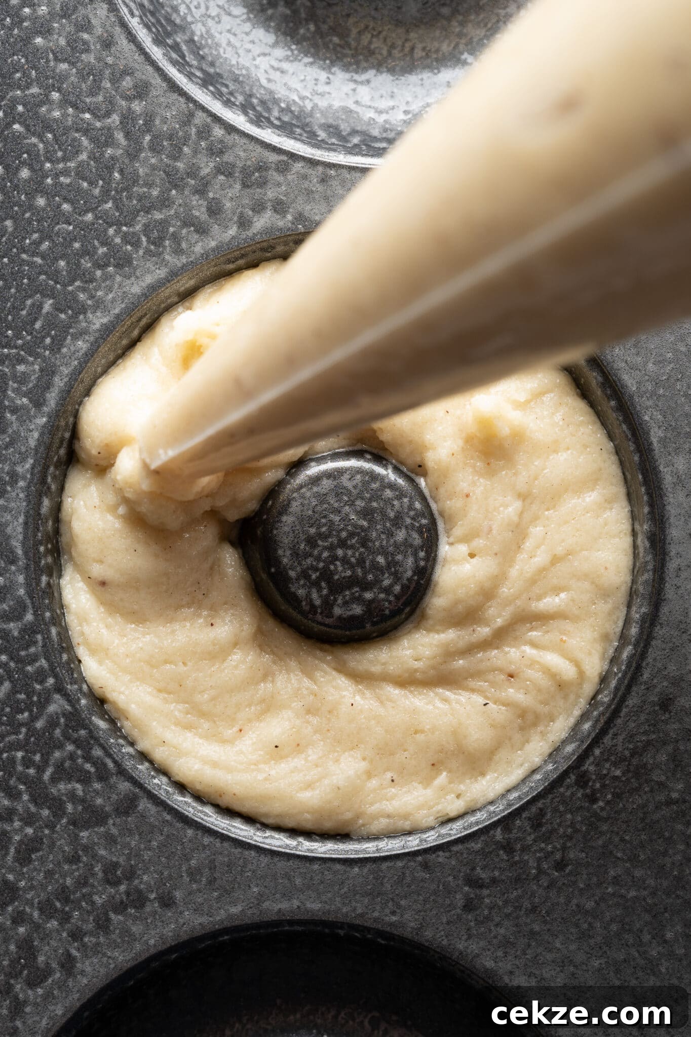A donut pan being filled with keto donut batter from a piping bag. 