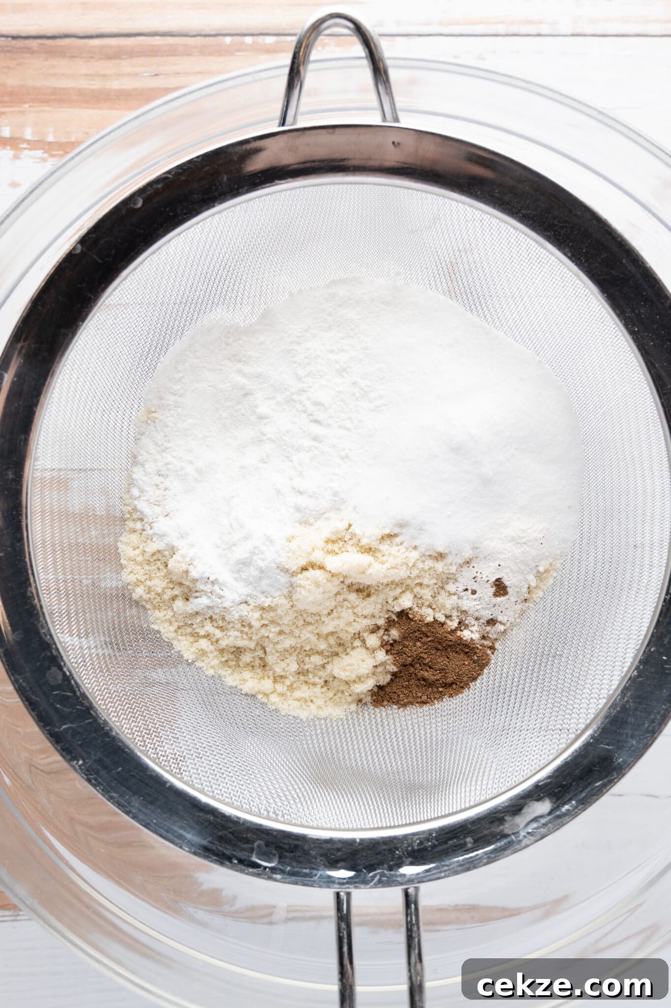 Low carb dry ingredients in a sifter sitting over a clear mixing bowl. 