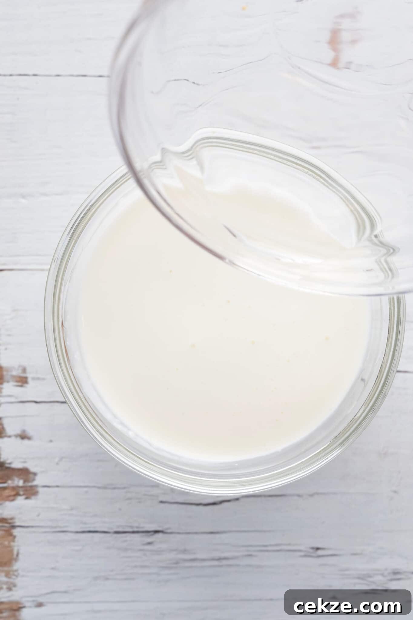 A bowl of heavy cream with vinegar being poured in.