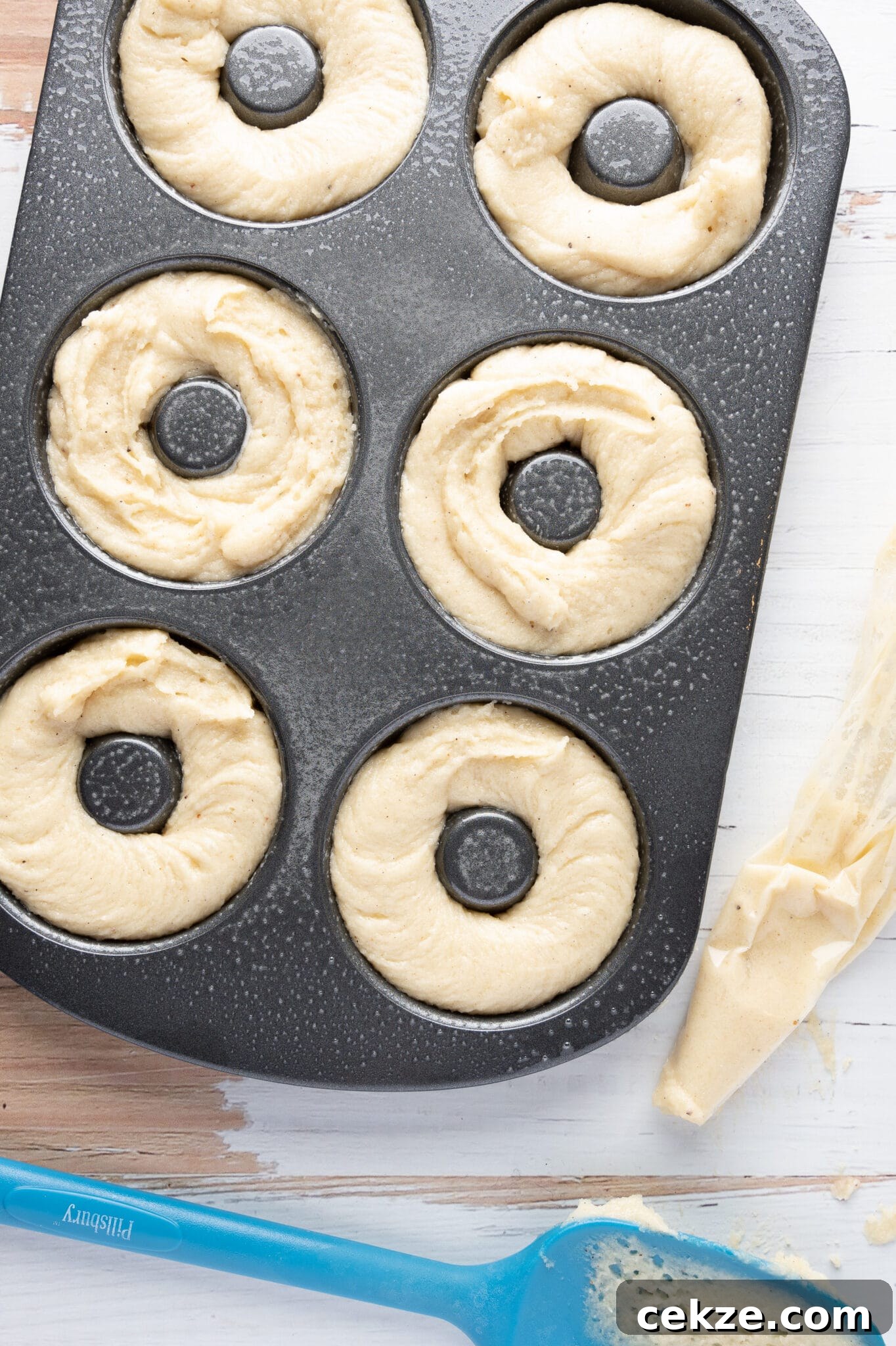 A donut pan filled with low carb donut batter.  An empty piping bag and batter coated spoon rest next to the pan. 