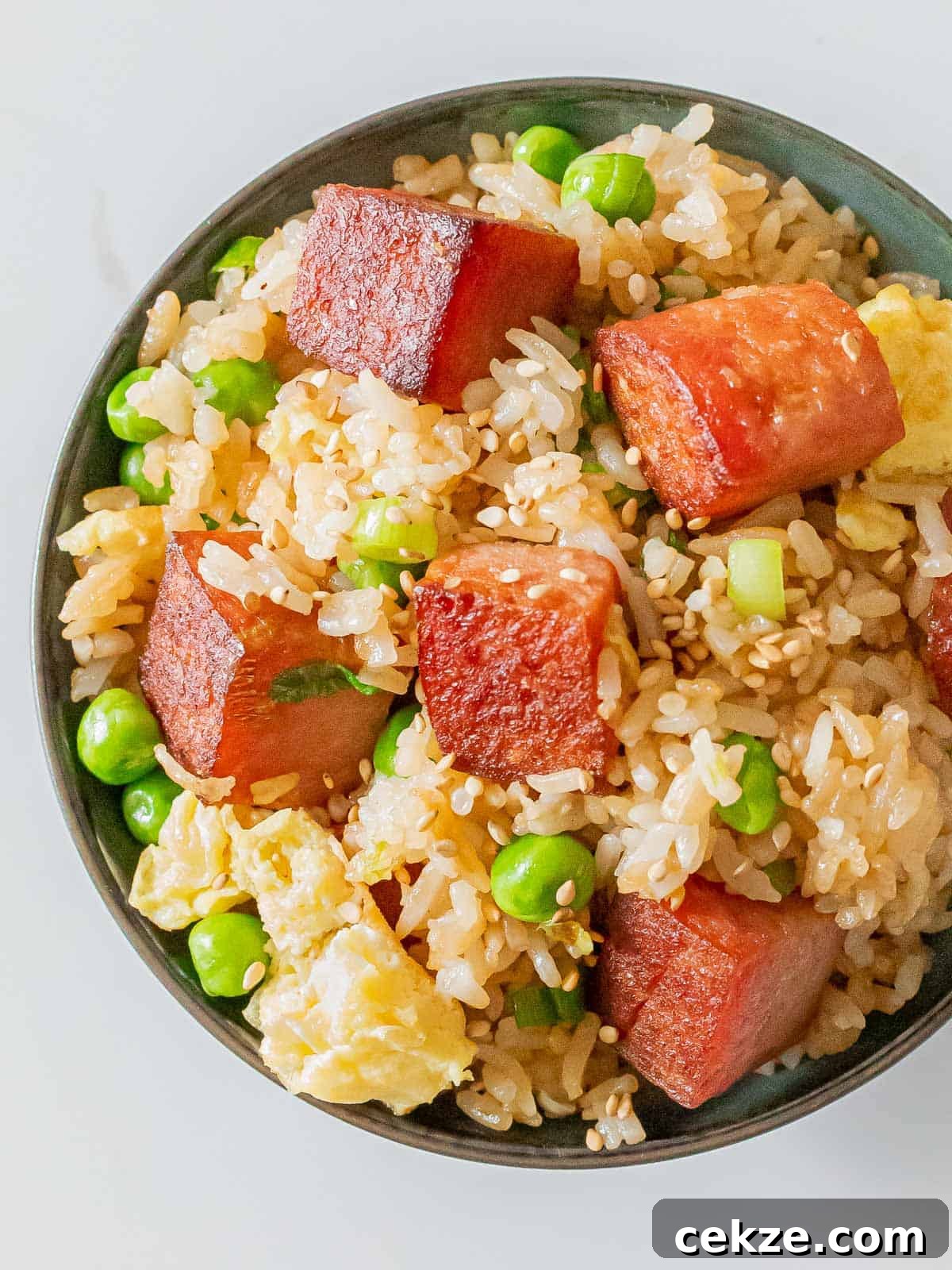 bowl of spam fried rice with crispy cubes of spam, eggs, green peas, and sesame seeds