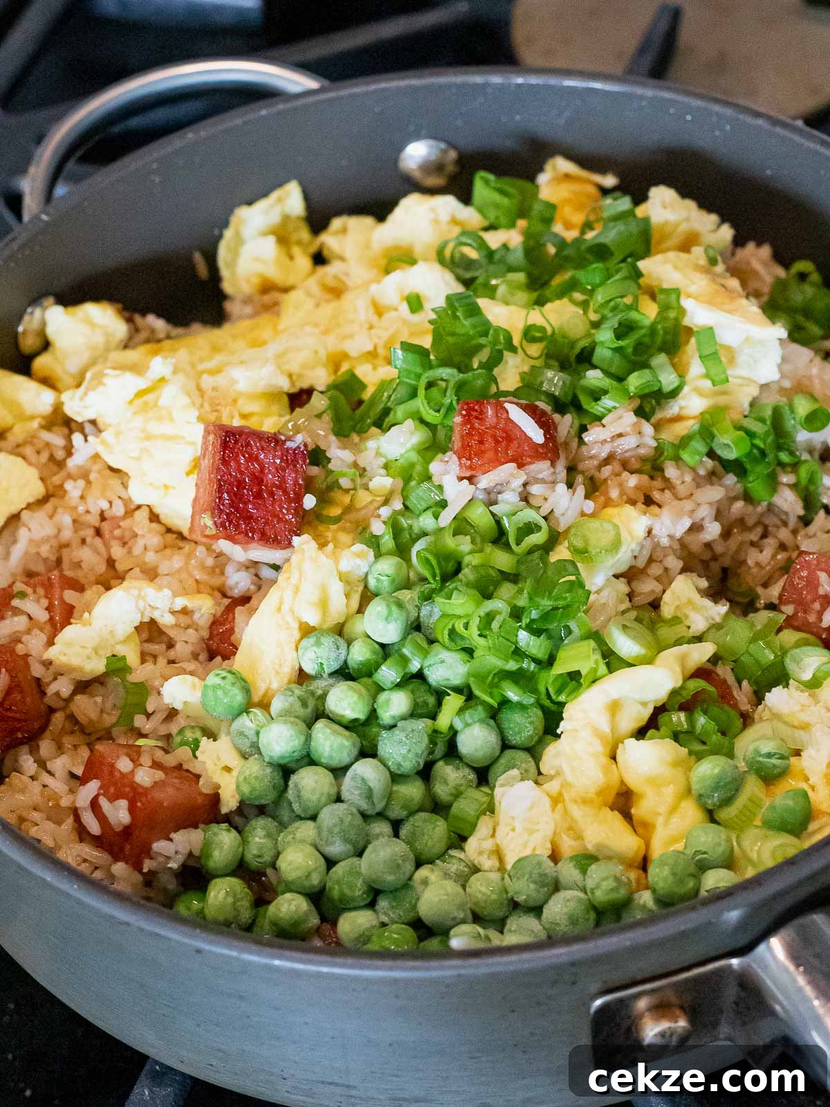 ingredients for spam fried rice in a nonstick pan including green peas and scallions