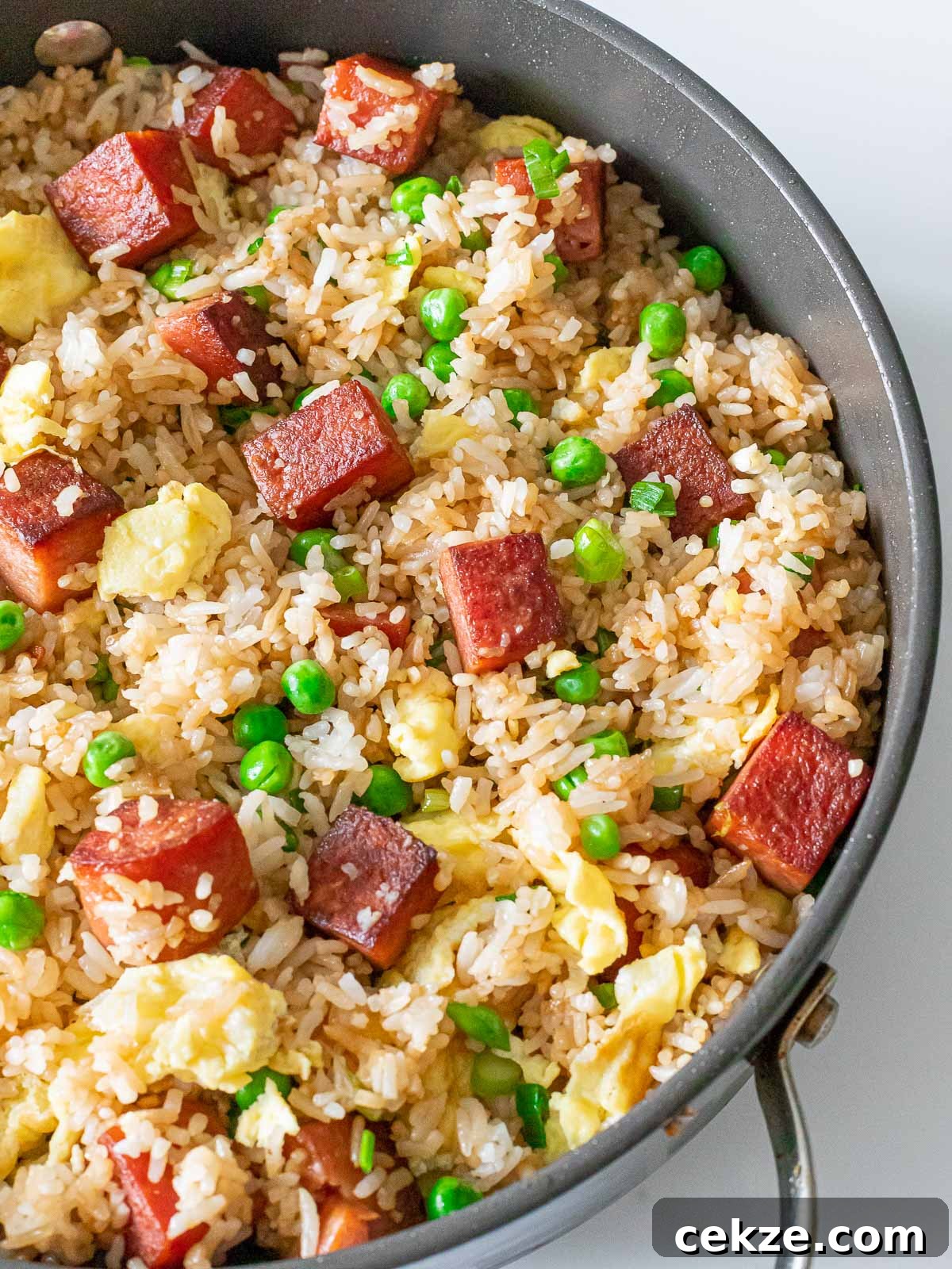 overhead of spam fried rice with pan fried spam, eggs, and green peas in a pan