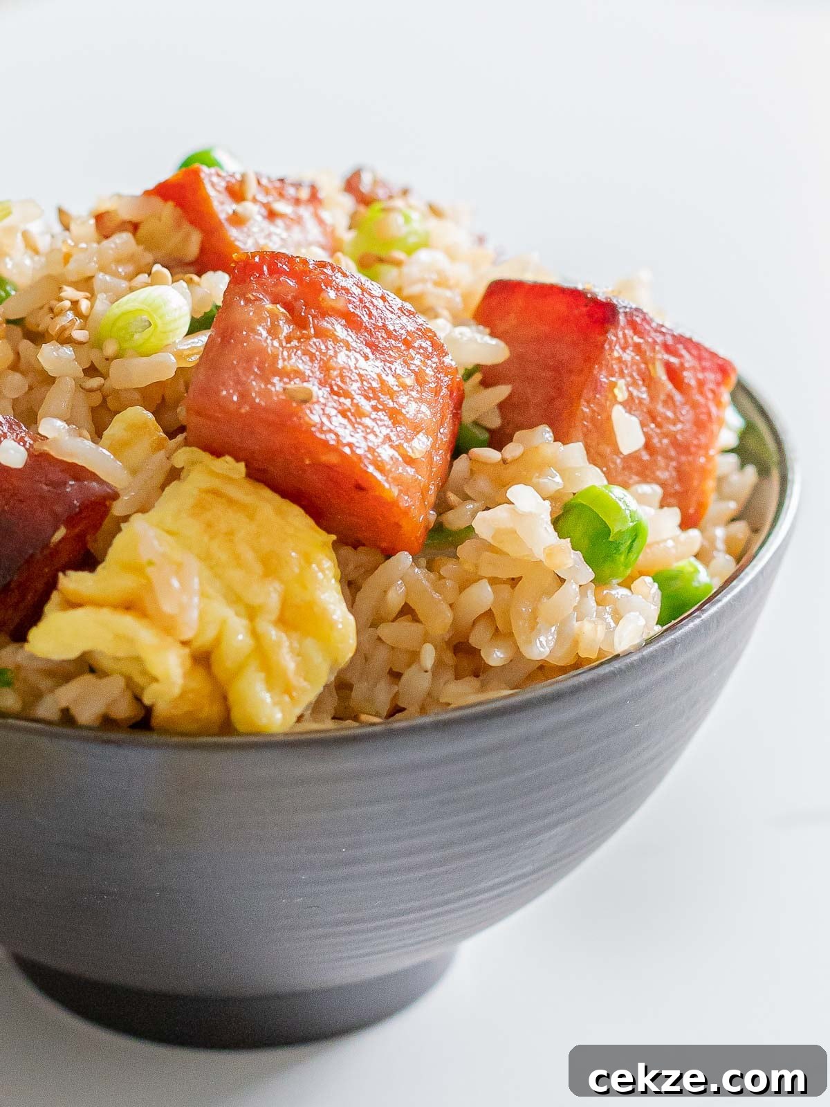 close up of spam fried rice with eggs, green peas, and rice in a dark bowl