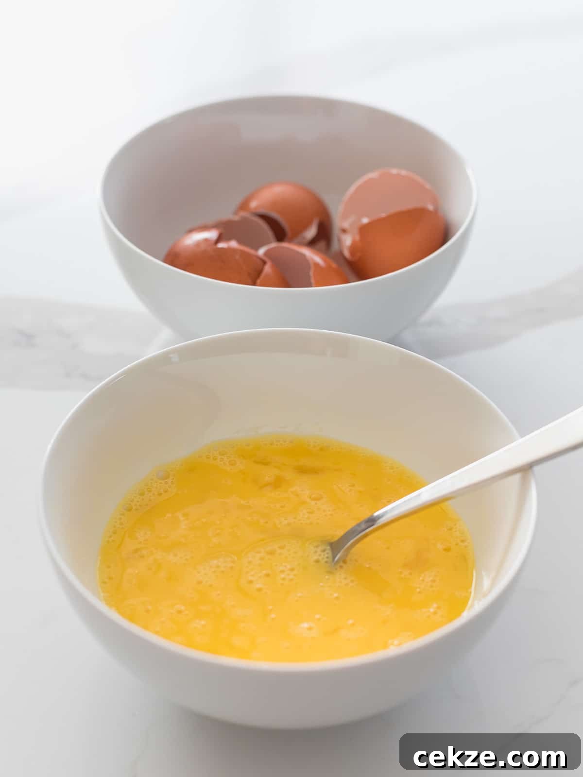 bowl of beaten eggs with a silver fork next to a bowl filled with egg shells