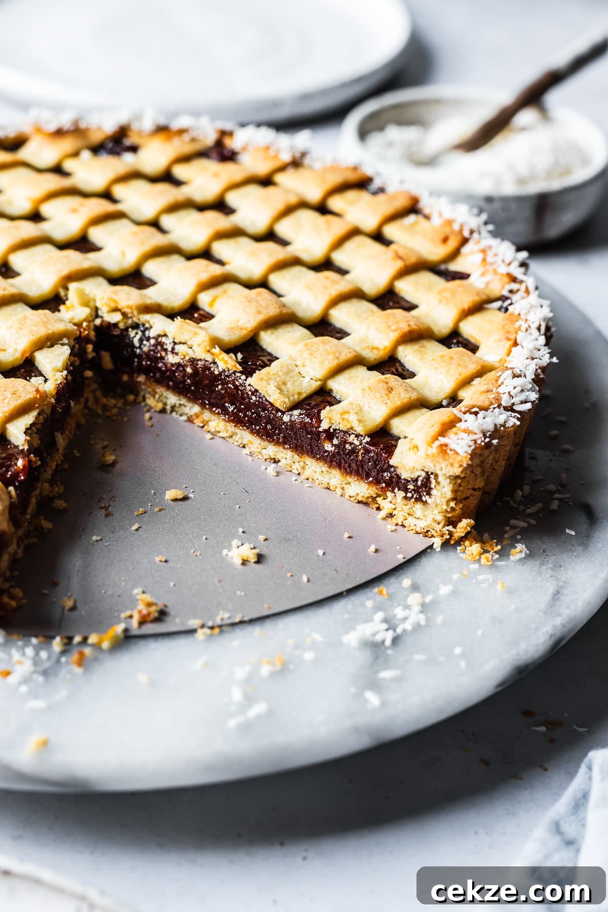 A quince tart with lattice top and border of dessicated coconut. There are a few slices missing, revealing the base crust and filling.