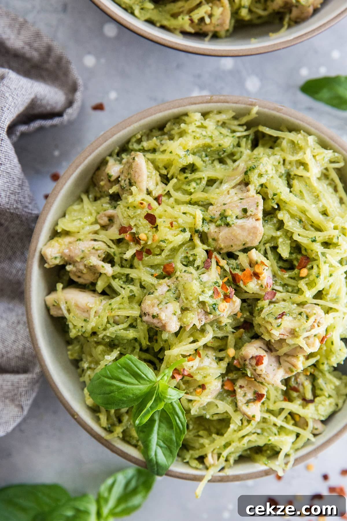 Top Chicken Thigh Recipes for Flavorful Weeknight Dinners 12 Close up top down image of two bowls of chicken pesto spaghetti squash with basil leaves and red pepper flakes for garnish.