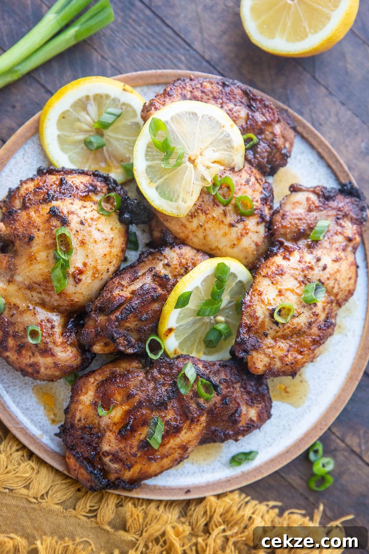 Top Chicken Thigh Recipes for Flavorful Weeknight Dinners 13 Top down plate of Mediterranean chicken sprinkled with green onions and slices of lemon on a rustic wooden background.