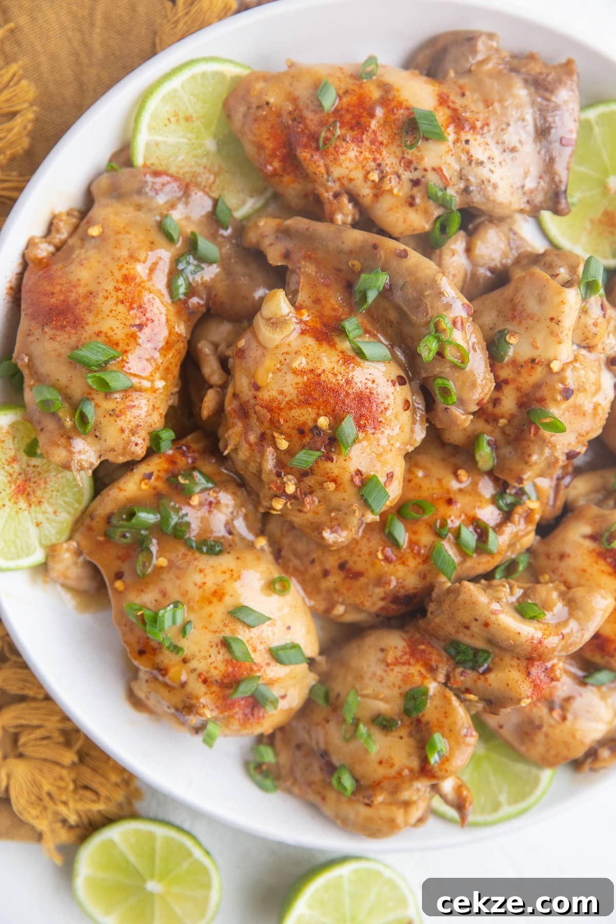 Top Chicken Thigh Recipes for Flavorful Weeknight Dinners 16 Top down white plate of cooked chicken thighs sprinkled with green onions and slices of limes all around.