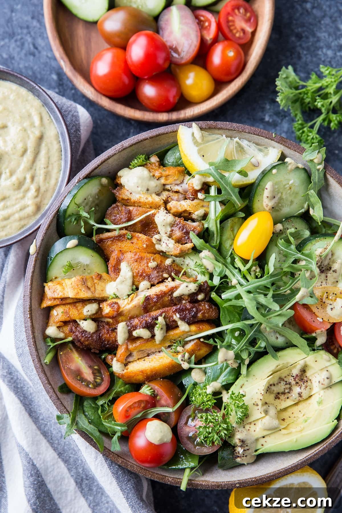 Top Chicken Thigh Recipes for Flavorful Weeknight Dinners 3 Big bowl of crispy chicken arugula salad with lemon tahini dressing, cherry tomatoes, avocado and more.