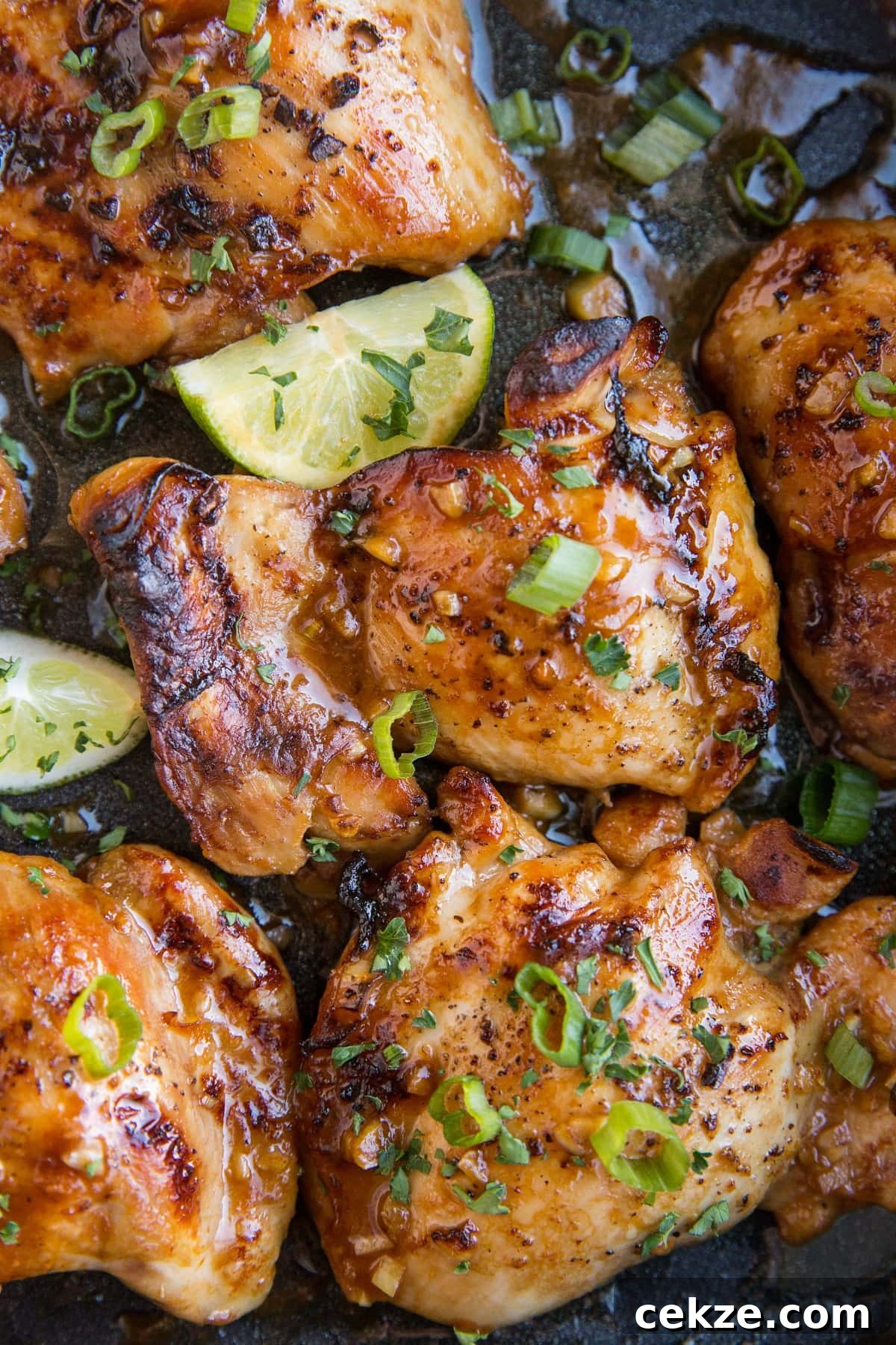Top Chicken Thigh Recipes for Flavorful Weeknight Dinners 7 Close up image of Asian Boneless Baked Chicken Thighs with green onion sprinkled on top and some limes