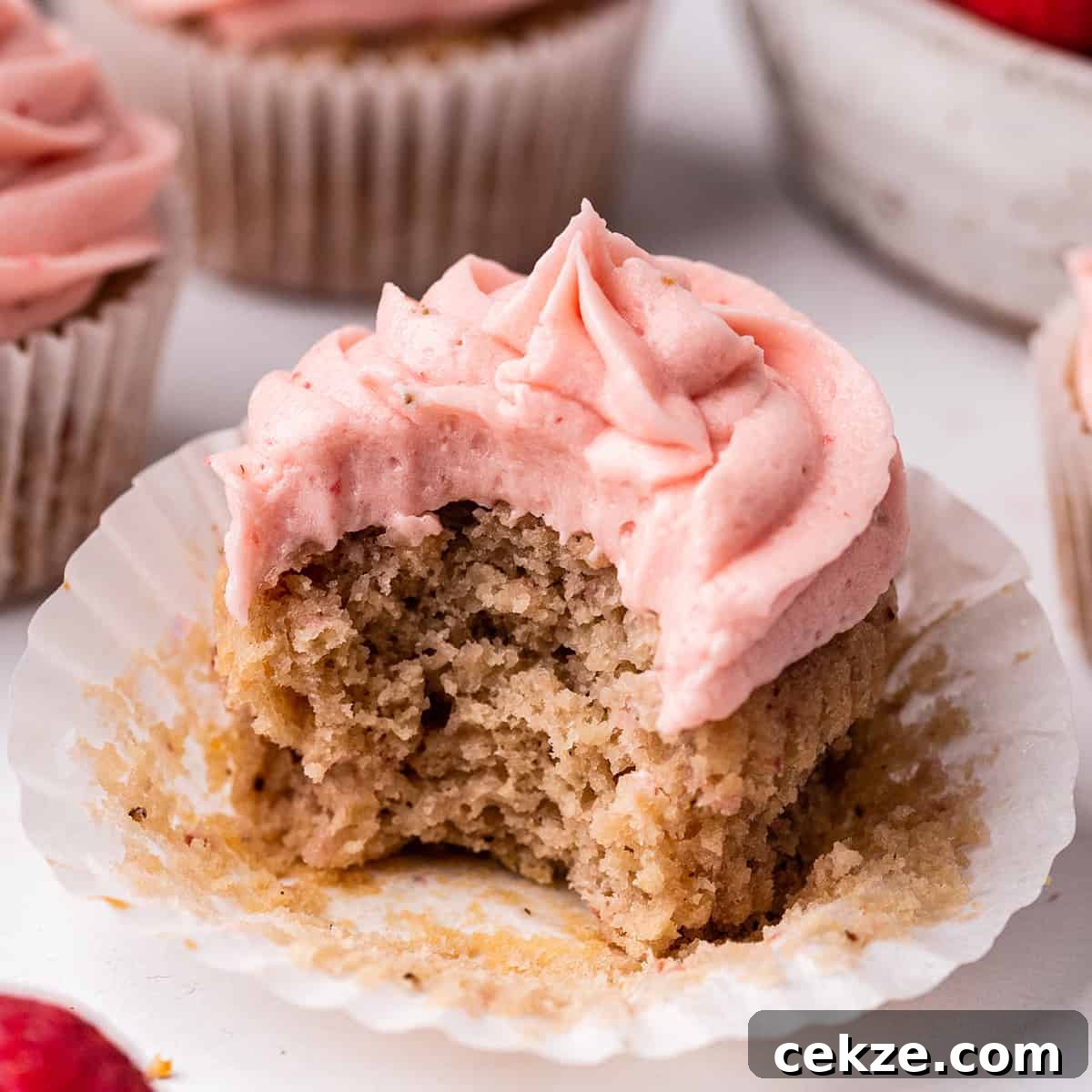 a frosted Strawberry Cupcake in a wrapper with a bite taken out of it