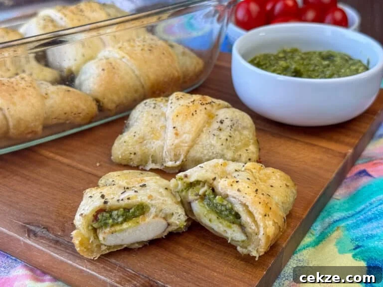 Flavorful layer of basil pesto coating mozzarella cheese wrapped in a crescent roll and cut open on a wooden board with the full baking dish and more pesto in the background.