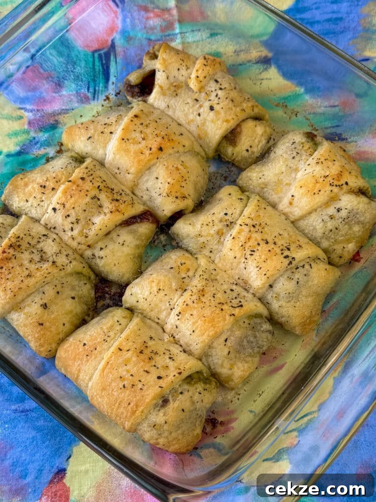 Overhead view of a baking dish full of golden brown pesto crescent rolls with mozzarella cheese and baked in butter to make a warm and delicious appetizer on a pastel napkin.