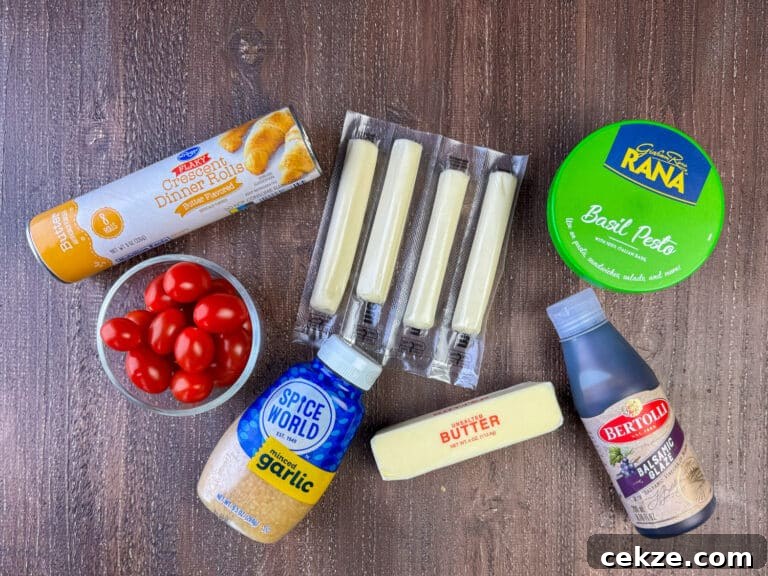 Ingredients to make pesto rolls are crescent dinner rolls, mozzarella cheese sticks, basil pesto, balsamic glaze, butter, garlic and cherry tomatoes on a wooden counter top.