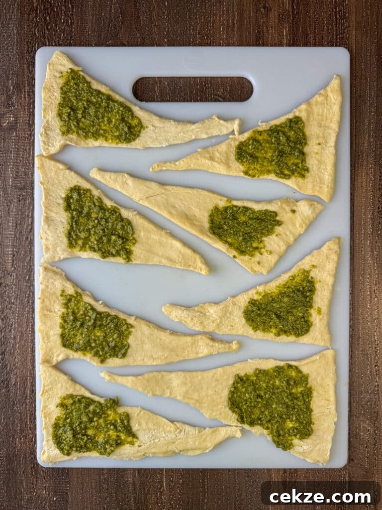 Pesto spread over triangular pieces of crescent dough laying on a cutting board.