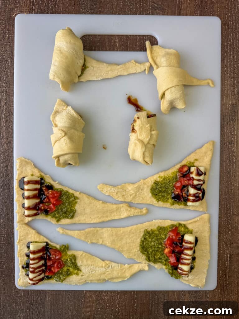 Several crescent rolls partially rolled up on a white cutting board showing how to make pesto crescent rolls.