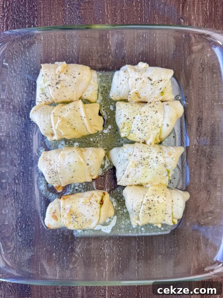 Crescent rolls filled with mozzarella cheese, garlic and pesto in an 8 x 8 glass baking dish and coated in melted butter.