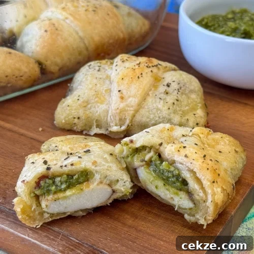 Warm, flaky crescent roll baked with a filling of pesto over caprese cheese cut in half with more rolls in the background on a wooden board.