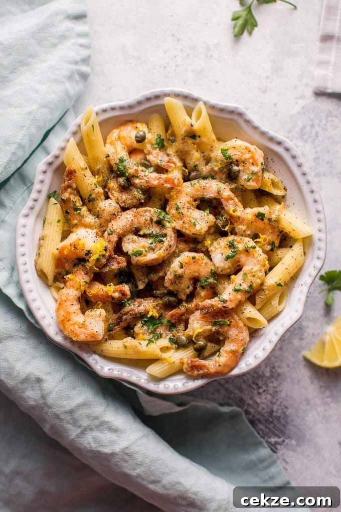 white bowl with easy shrimp piccata served over penne beside cloth napkin and lemon slice