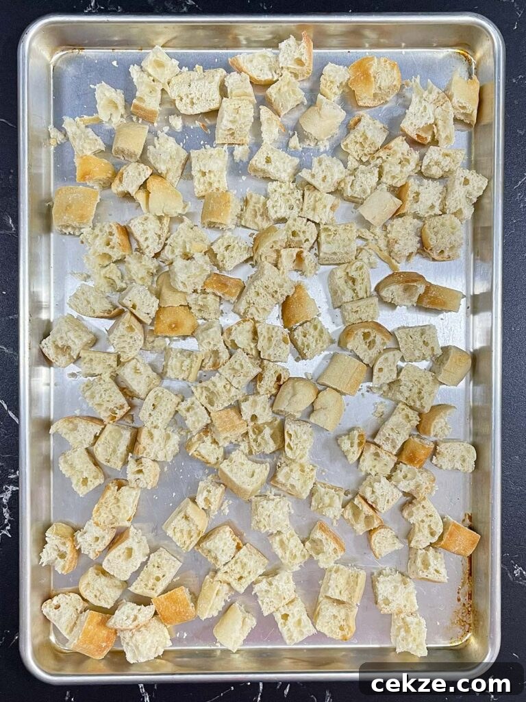 Cubed ciabatta bread spread on a baking sheet for drying.
