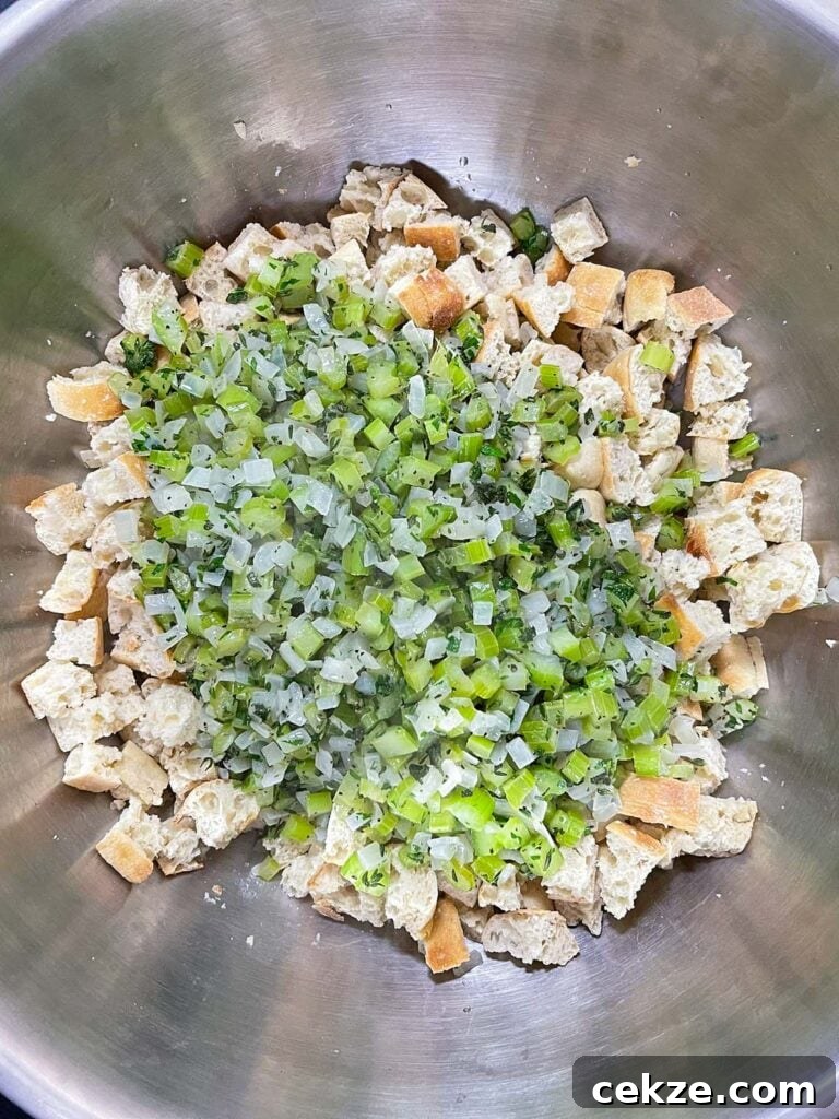 Cooked vegetables added to dried bread cubes in a mixing bowl before combining.