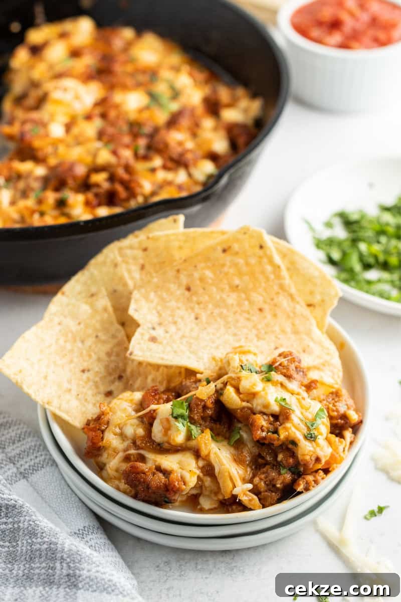 chorizo queso fundido on a small side plate with a couple of tortilla chips with the skillet of dip in the background