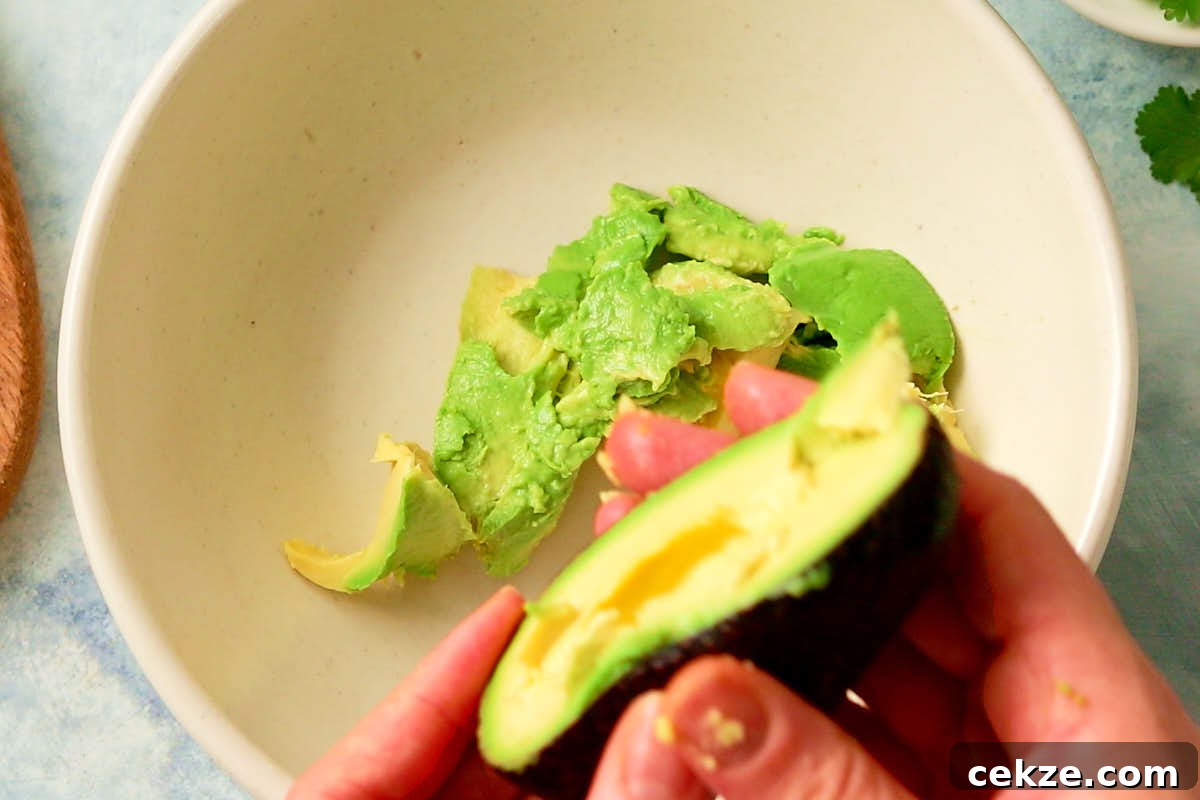 Scooping avocado flesh into a bowl for vegan guacamole.