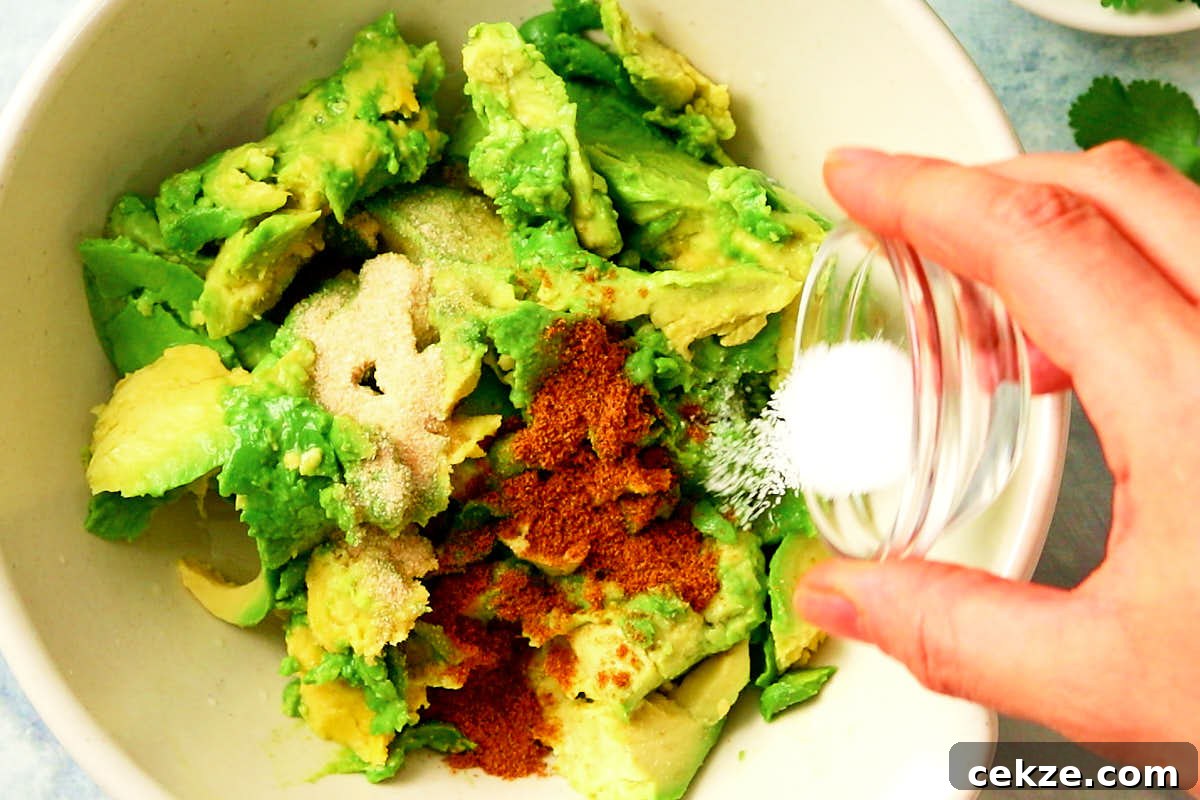 Adding spices to a bowl of avocado.