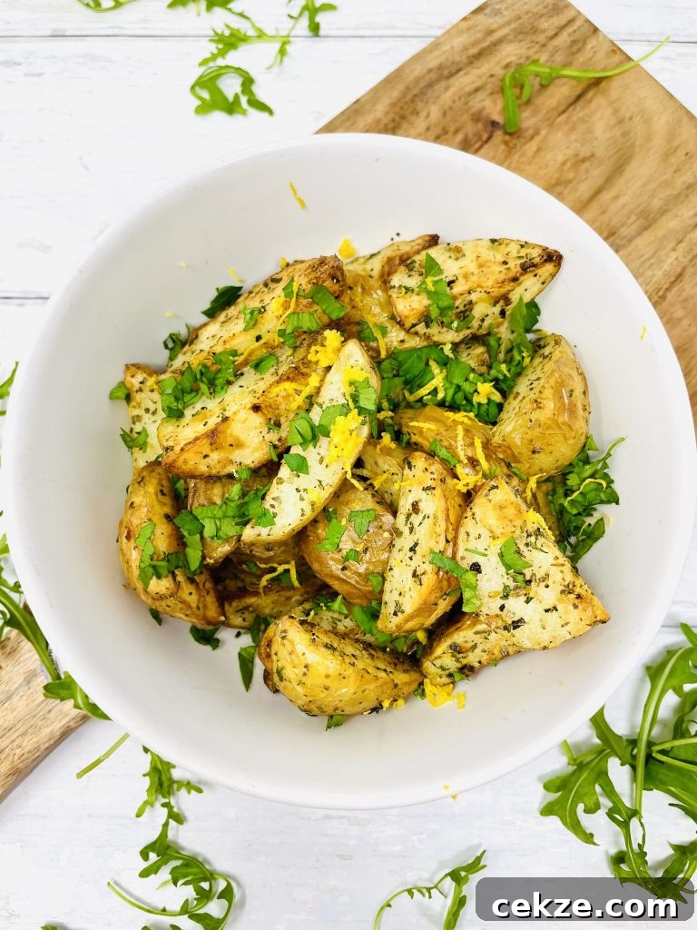 air fryer new potatoes with italian herbs served in a white bowl on a wooden board strewn with rocket leaves