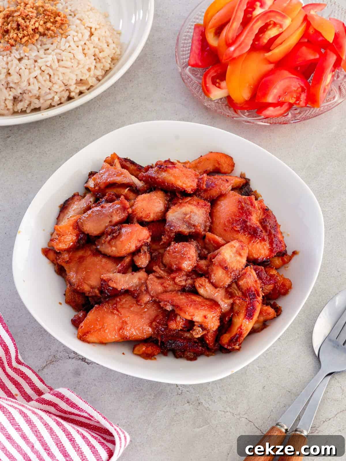 Chicken Tocino in a white serving bowl with garlic fried rice and sliced tomatoes in the background.