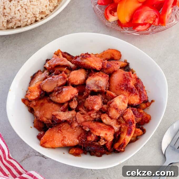 Chicken Tocino in a white serving bowl with garlic fried rice and sliced tomatoes in the background.