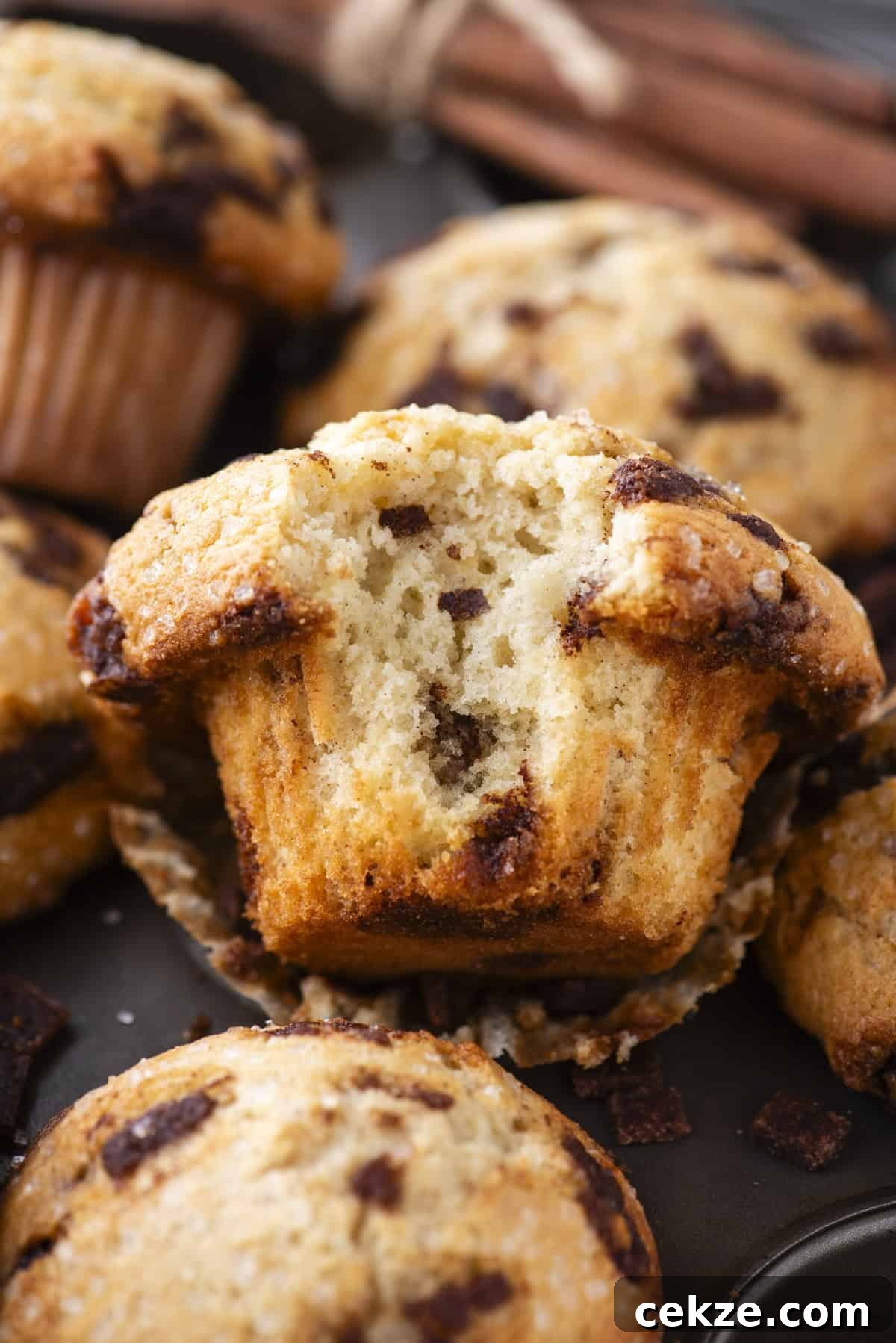 Cinnamon Baking Chips: Flavorful Mix-Ins for Cookies & Muffins 10 A close-up of cinnamon chip muffins, with one muffin cut in half to show its moist, fluffy texture and cinnamon chunks inside. Other whole muffins and cinnamon sticks are in the background.