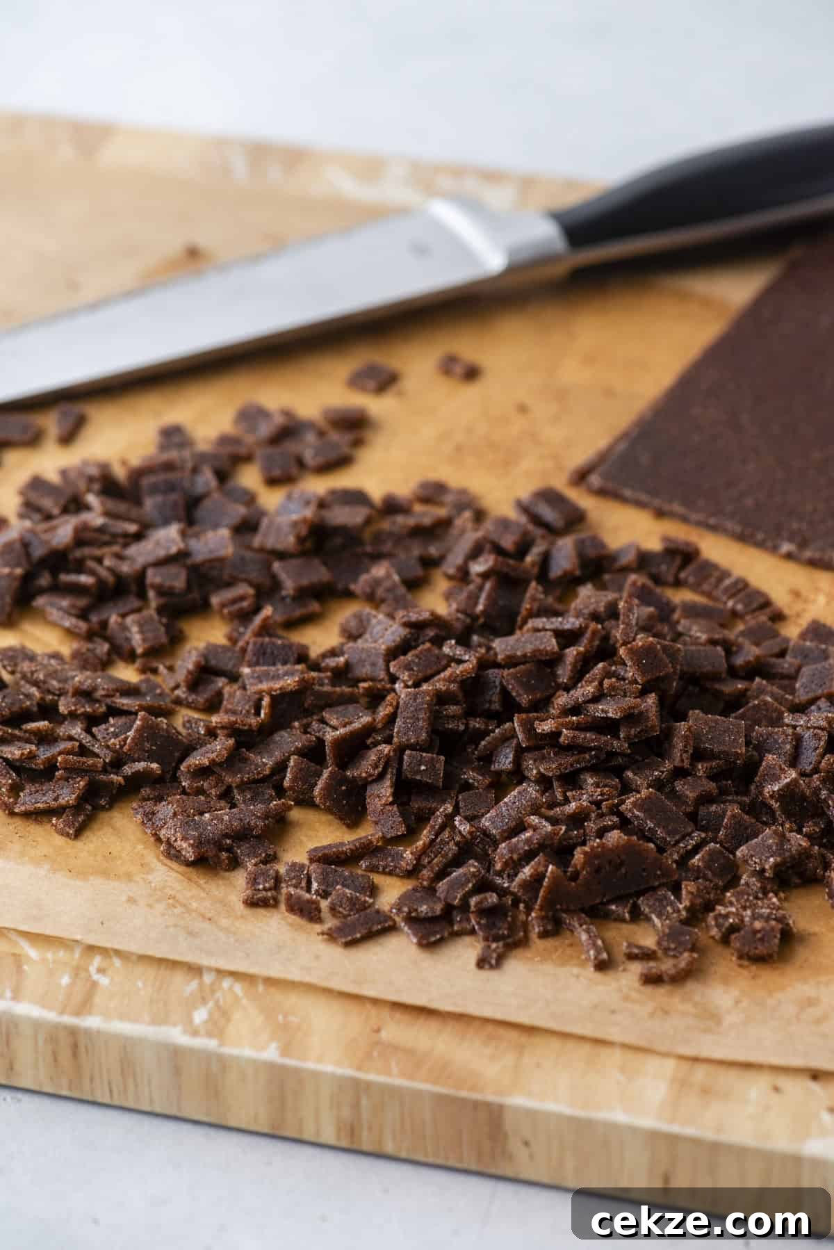 Cinnamon Baking Chips: Flavorful Mix-Ins for Cookies & Muffins 9 Small diced pieces of homemade cinnamon chips are scattered on a piece of parchment paper on a wooden cutting board, with a kitchen knife in the background.