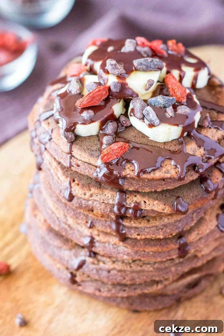 A stack of chocolate banana pancakes topped with banana slices and chocolate drizzle.