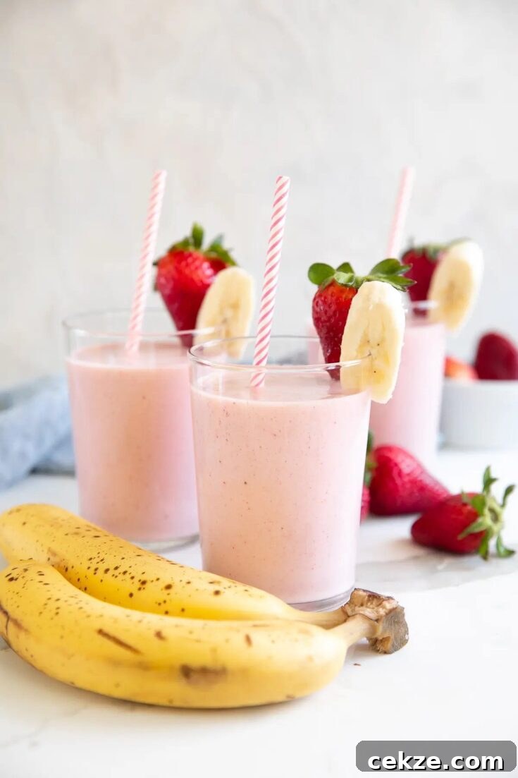 Pink strawberry banana smoothies, garnished with a slice of strawberry and banana.