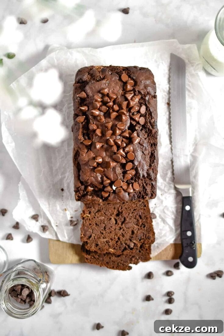 Overhead view of a loaf of double chocolate banana bread, next to a large knife, on a white marble table.