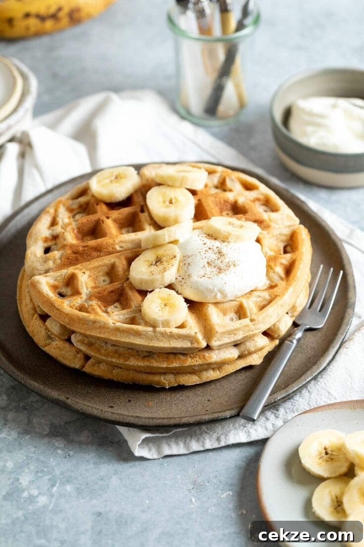 A stack of banana waffles topped with banana slices and whipped cream.