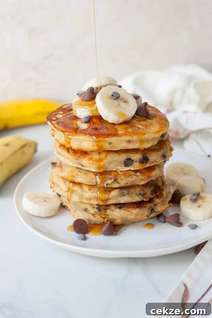 A stack of banana chocolate chip pancakes with a drizzle of maple syrup on top.