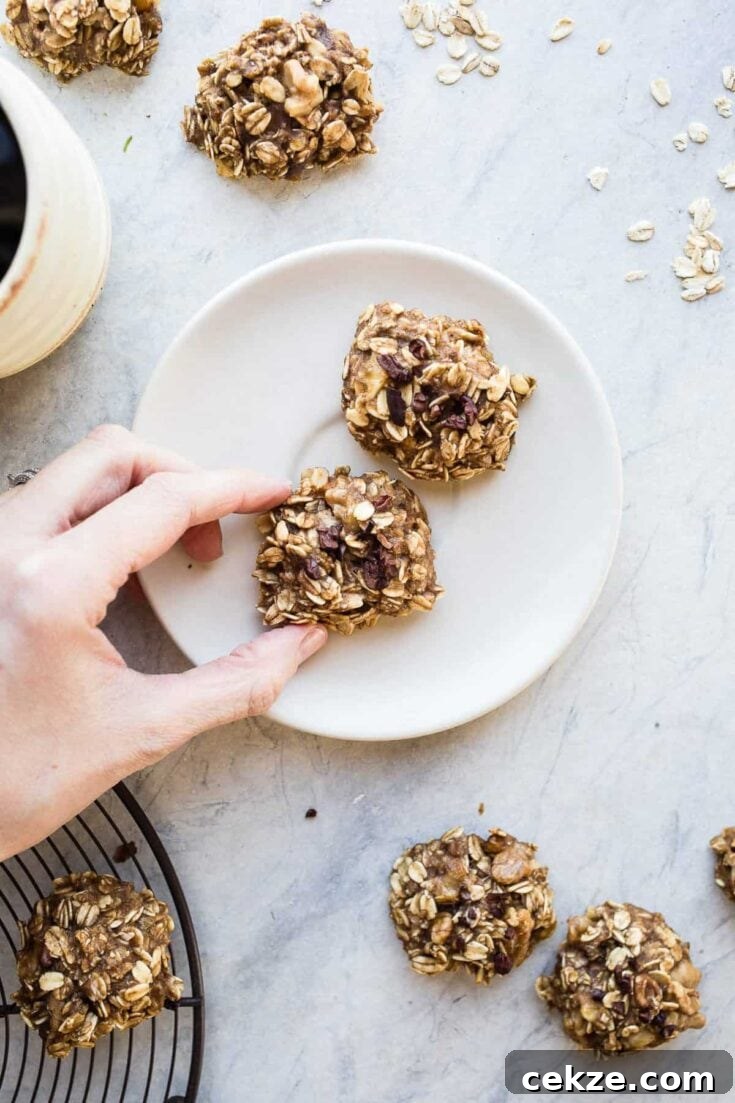 Overhead view of a hand grabbing a banana oatmeal cookie from a small white plate.