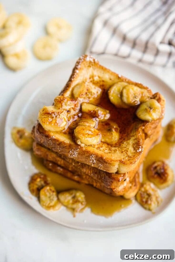 A stack of banana french toast, topped with banana slices and maple syrup.