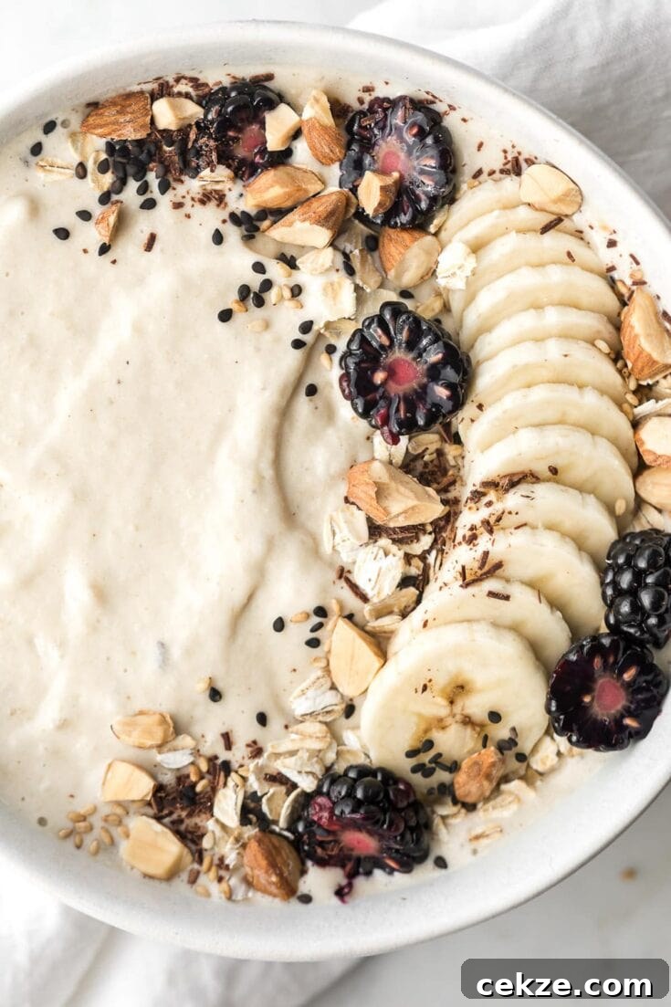 A banana smoothie bowl topped with banana slices, almonds, and blackberries.