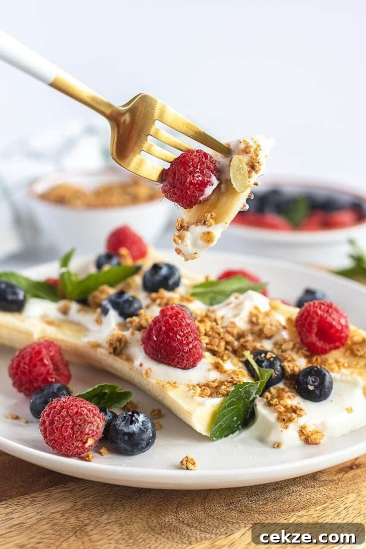 A fork holding a bite of breakfast banana split topped with granola and fresh berries.