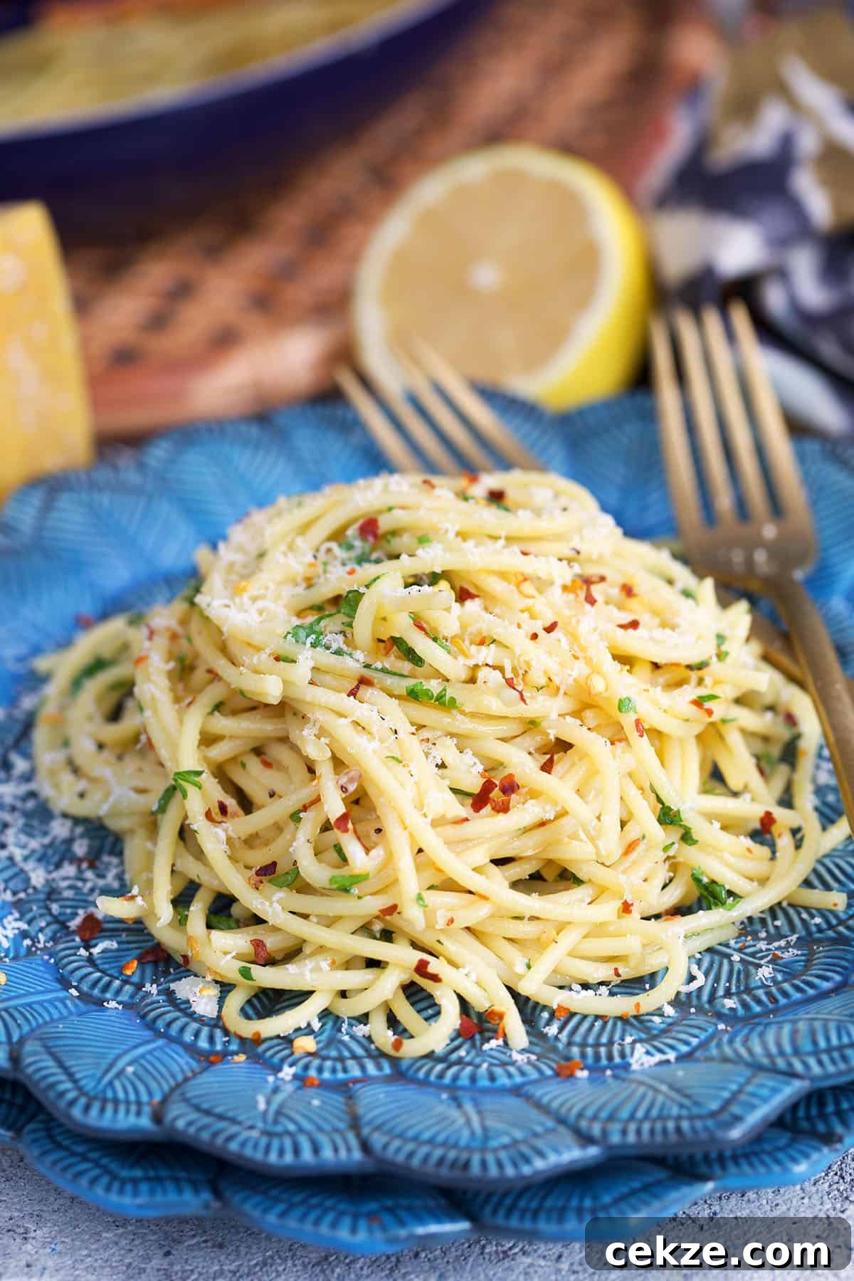 Classic Spaghetti Aglio e Olio: Simple Garlic Olive Oil Pasta Recipe 2 Spaghetti aglio e olio plated on a blue plate with a gold fork and topped with cheese.