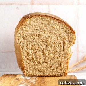 Homestyle Whole Wheat Sandwich Bread Recipe for Families 13 Halved whole wheat bread loaf on a wooden board. Tile background.