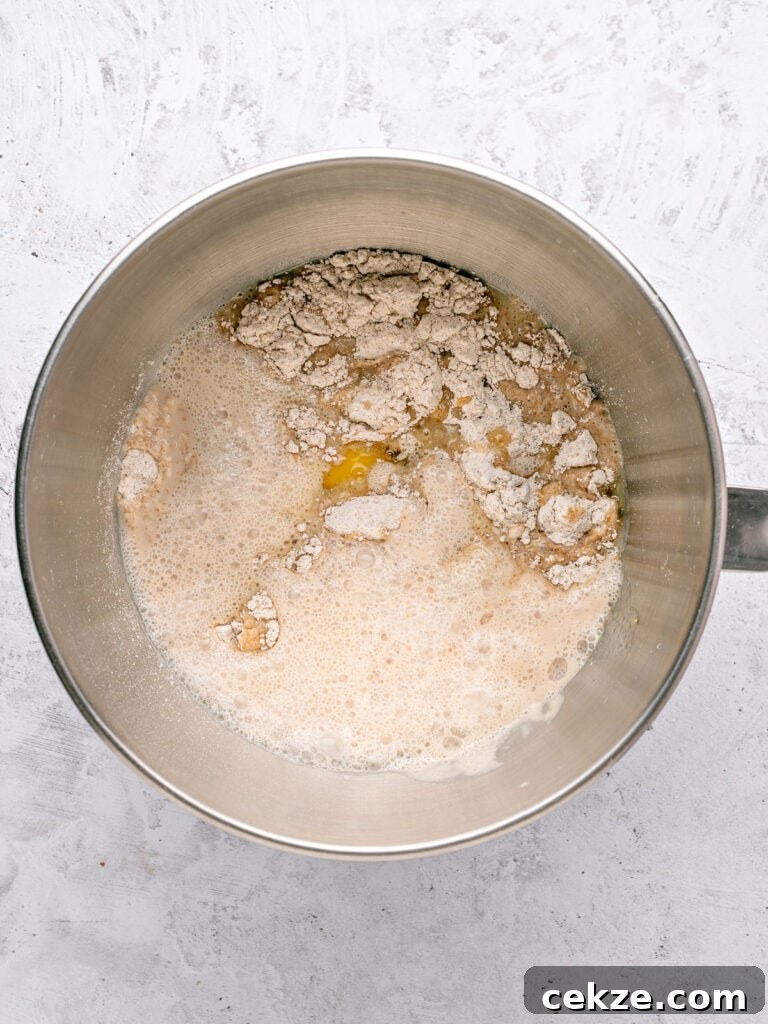 Homestyle Whole Wheat Sandwich Bread Recipe for Families 5 Yeast mixture, wet ingredients and flours in a metal bowl. Light gray background.