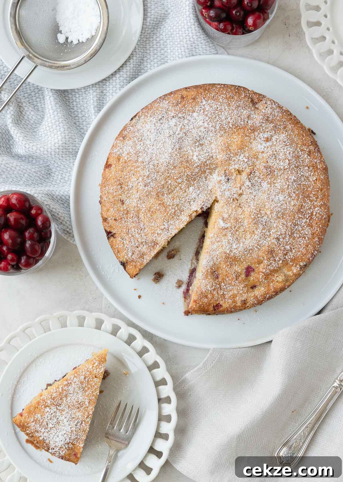 A nantucket cranberry pie on a plate, with a slice out, cranberries beside