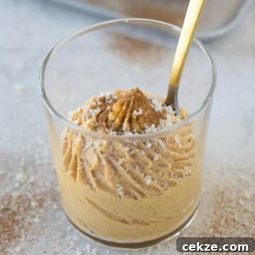 A glass of creamy pumpkin mousse dusted with cinnamon with a gold spoon.